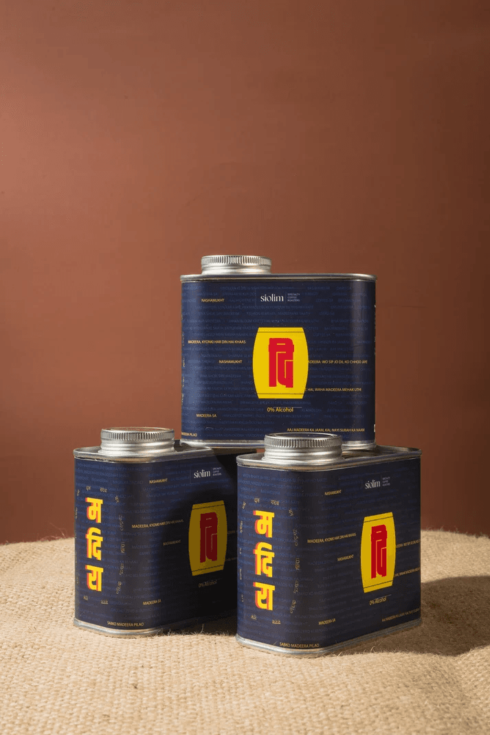 Three navy Siolim coffee tins with a yellow and red Madeera label, stacked against a terracotta wall